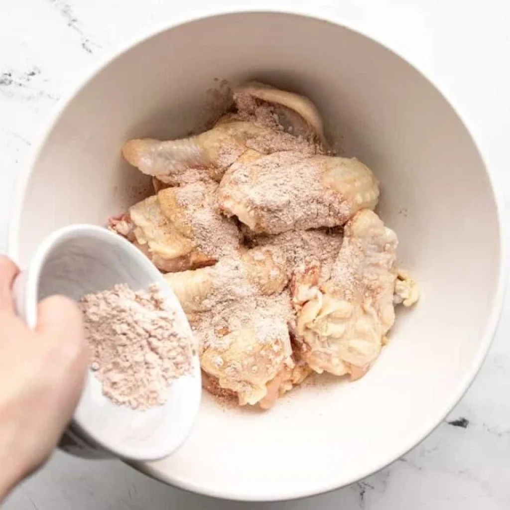 ailes de poulet enrobées d'huile et de mélange épices-fécule de maïs dans un bol avant cuisson au four