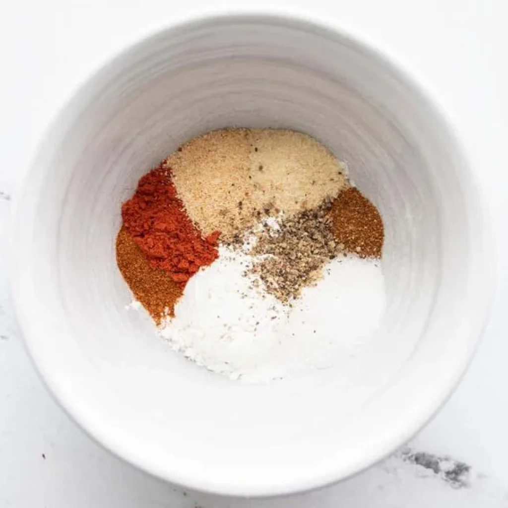 mélange d'épices dans un bol pour assaisonner les ailes de poulet au four : paprika, ail en poudre, fécule de maïs