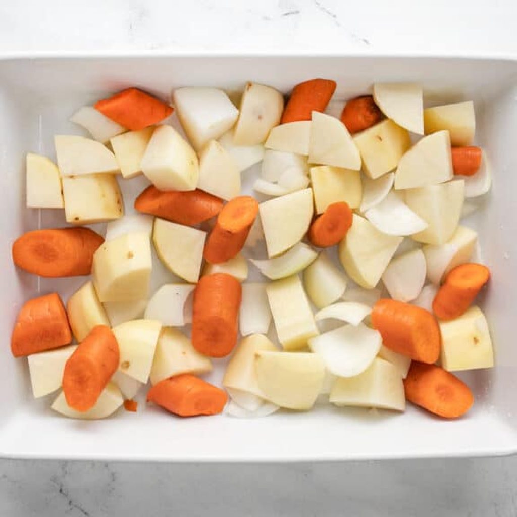 Des carottes, des pommes de terre et des oignons coupés en morceaux dans un plat de cuisson, prêts à être rôtis avec un poulet.