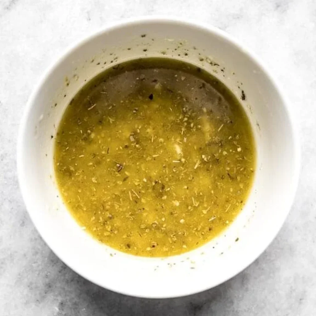 Préparation d'une marinade à l'huile d'olive, avec des herbes aromatiques et peut-être de l'ail, pour un poulet grec au four savoureux.