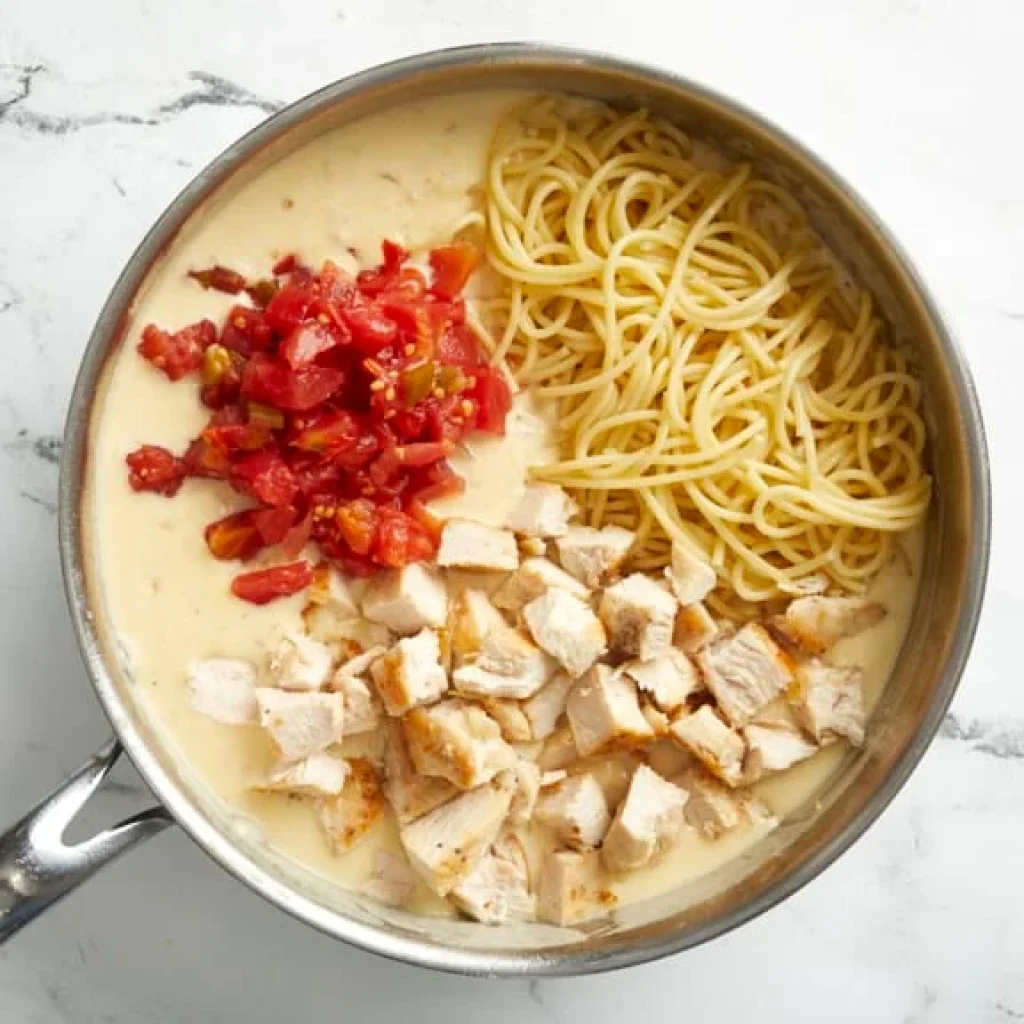 spaghetti, poulet et tomates dans une sauce crémeuse prêts à être mélangés pour le gratin de spaghetti au poulet