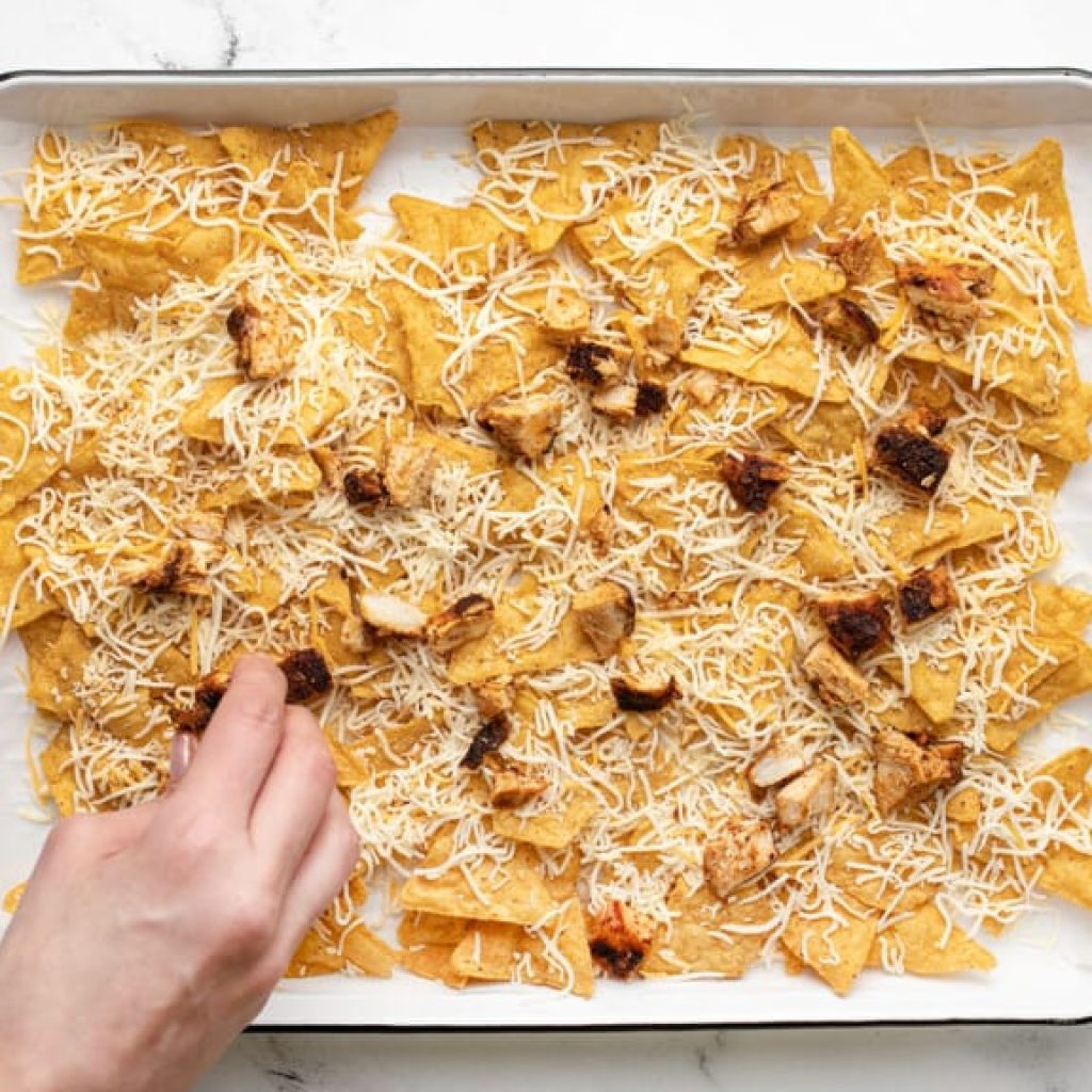 nachos au poulet montés en deux couches sur une plaque avec fromage avant passage au four