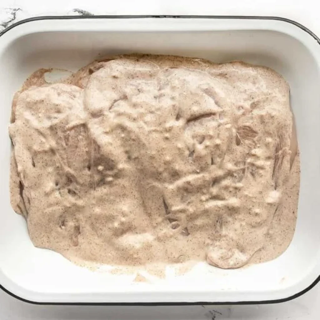 Préparation d'une marinade de yaourt pour poulet, avec des poitrines de poulet recouvertes de sauce