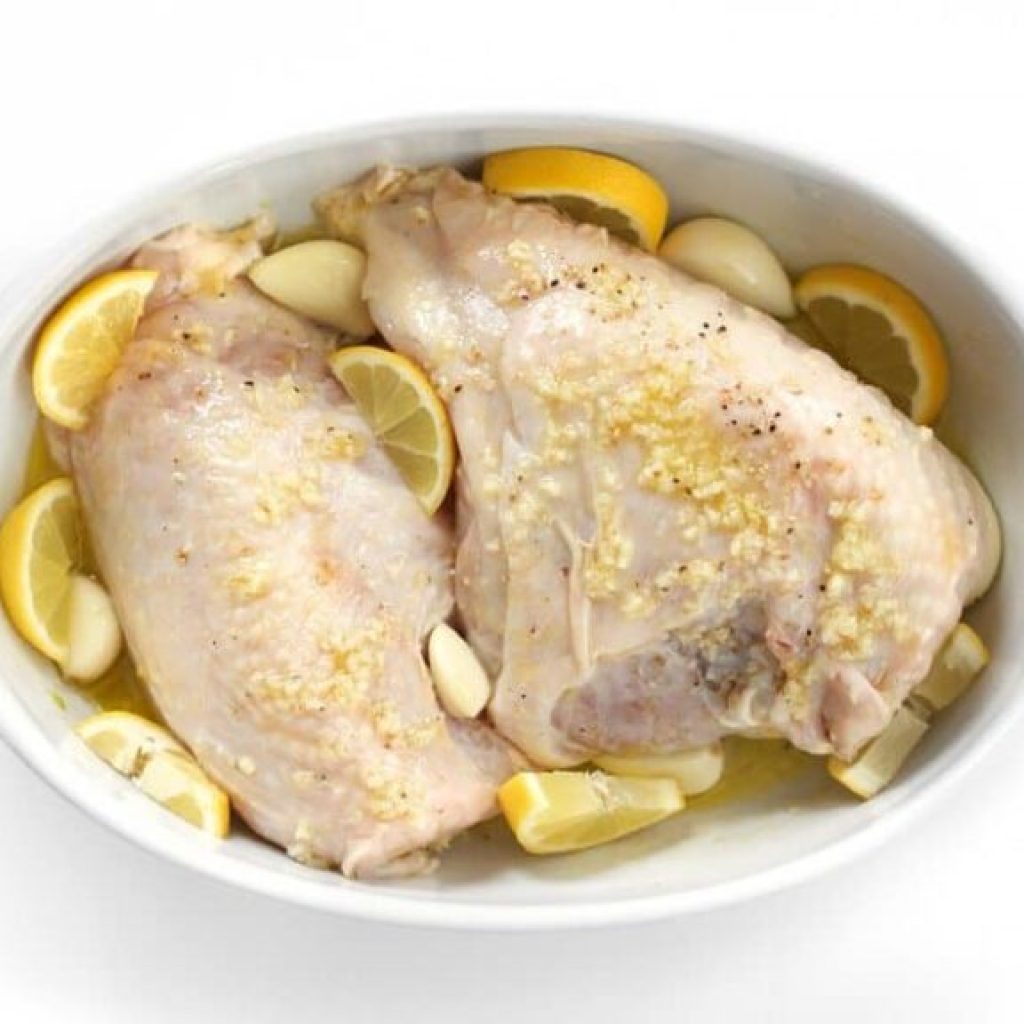 blanc de poulet basse température prêt à rôtir dans un plat avec tranches de citron et gousses d'ail entières
