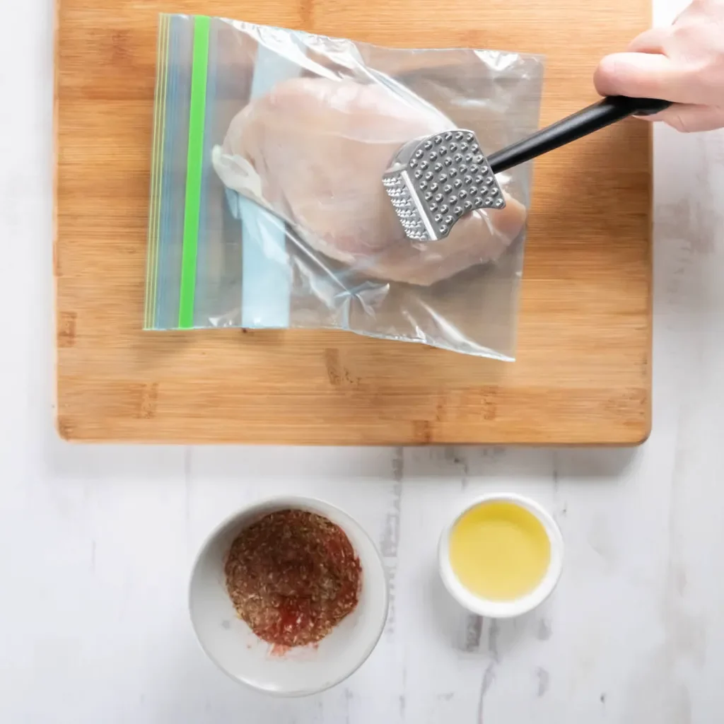 aplatir la poitrine de poulet avec un rouleau à pâtisserie pour une cuisson uniforme au four