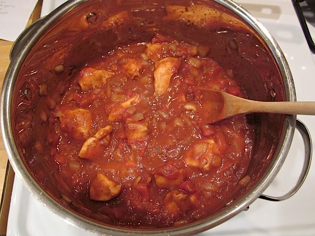 Poulet mijotant dans une sauce tomate, une cuillère en bois est posée sur le bord, préparation poulet au beurre