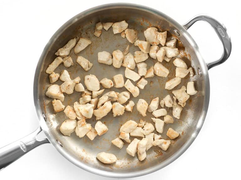 Poulet coupé en morceaux en train de cuire dans une casserole en acier inoxydable, pour une recette de casserole de poulet, brocoli et riz