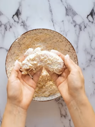 Un batonnet de poulet pane est tenu par deux mains edited
