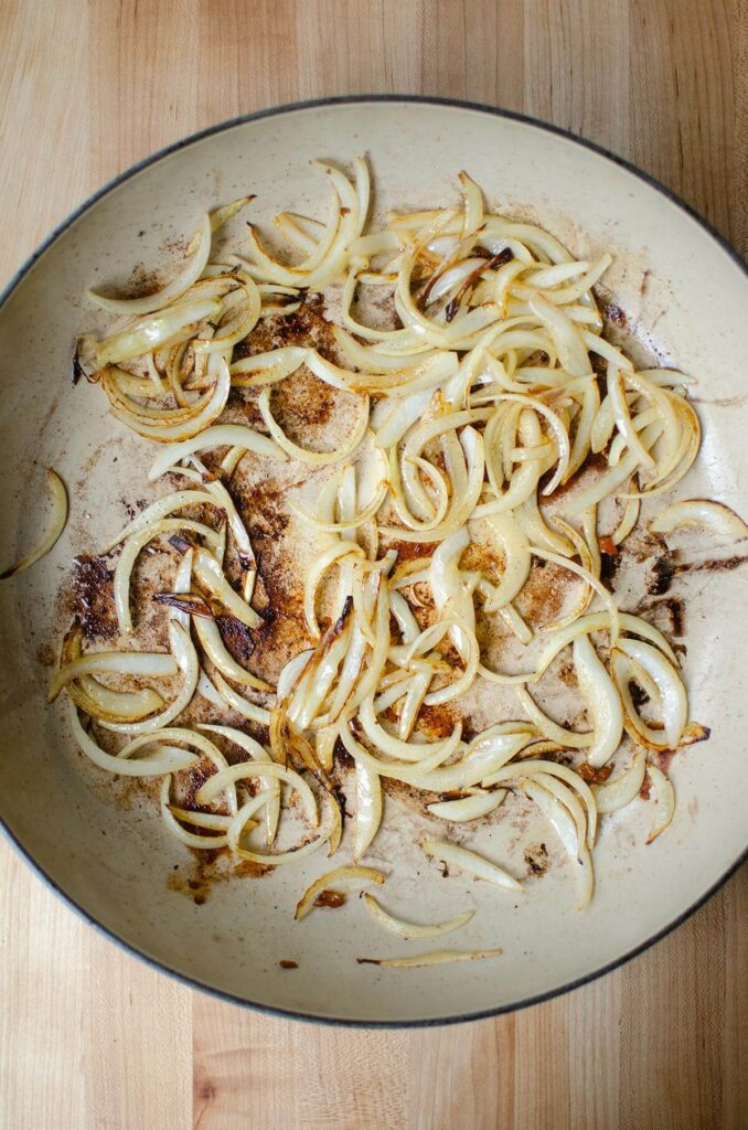 "Oignons émincés, en cours de cuisson dans une poêle. Étape de la préparation du poulet basquaise à l'ancienne."