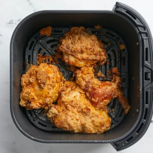 Savourez le goût du poulet frit traditionnel avec moins d'huile et moins de calories en le cuisant à l'air. Cette image montre un panier de morceaux de poulet dorés et croustillants cuits dans une friteuse à air.