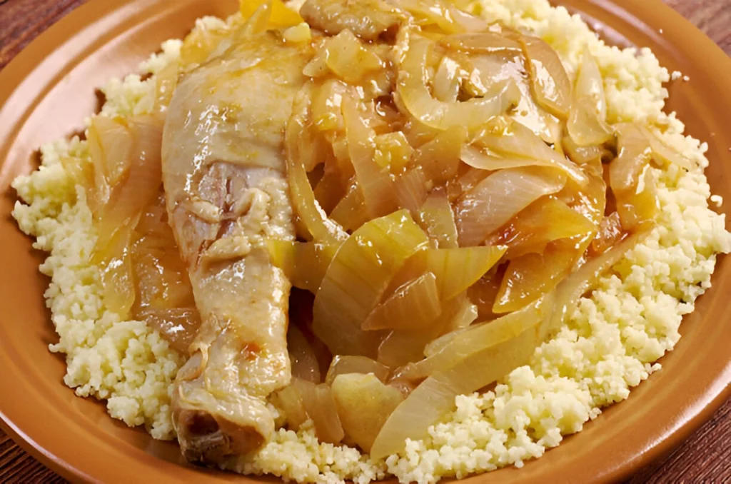 Un plat de poulet Yassa, spécialité du Sénégal, présenté sur une assiette. Le poulet est braisé dans une sauce d'oignons caramélisés et est servi sur un lit de couscous.