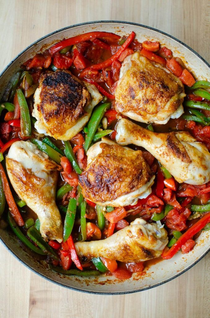 "Poivrons rouges et verts coupés en lamelles, ajoutés aux oignons dorés dans une poêle. Étape de la préparation du poulet basquaise à l'ancienne."