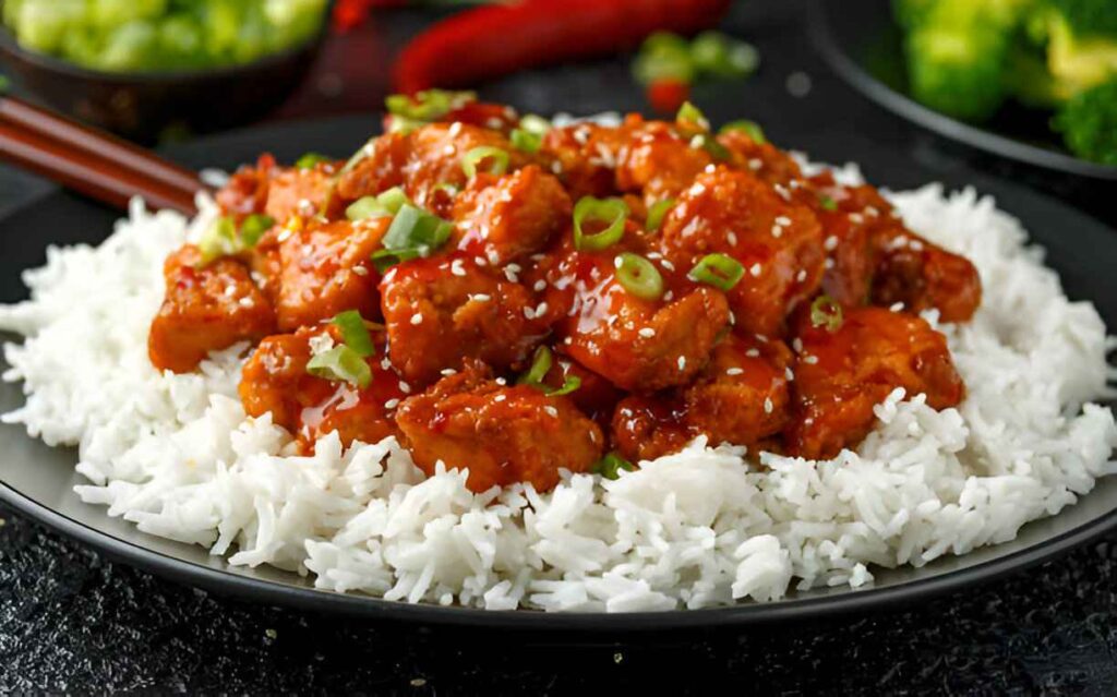 Gros plan sur un plat de poulet Général Tao servi sur un lit de riz blanc.
