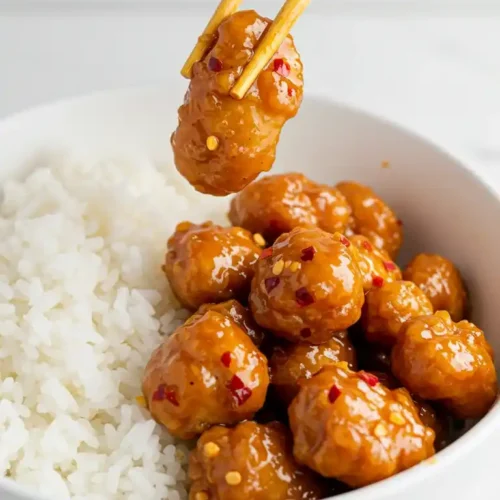 Poulet Général Tao cuit à l'air fryer, servi avec du riz. Une pièce est saisie avec des baguettes.