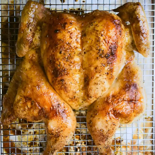 Un poulet-en-crapaudine doré, cuit à la perfection, repose sur une grille, sa peau croustillante parsemée d'herbes et d'épices.