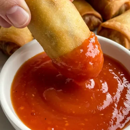 Gros plan sur un nem croustillant au poulet, trempé dans une sauce rouge vive. Recette pour nems au poulet.