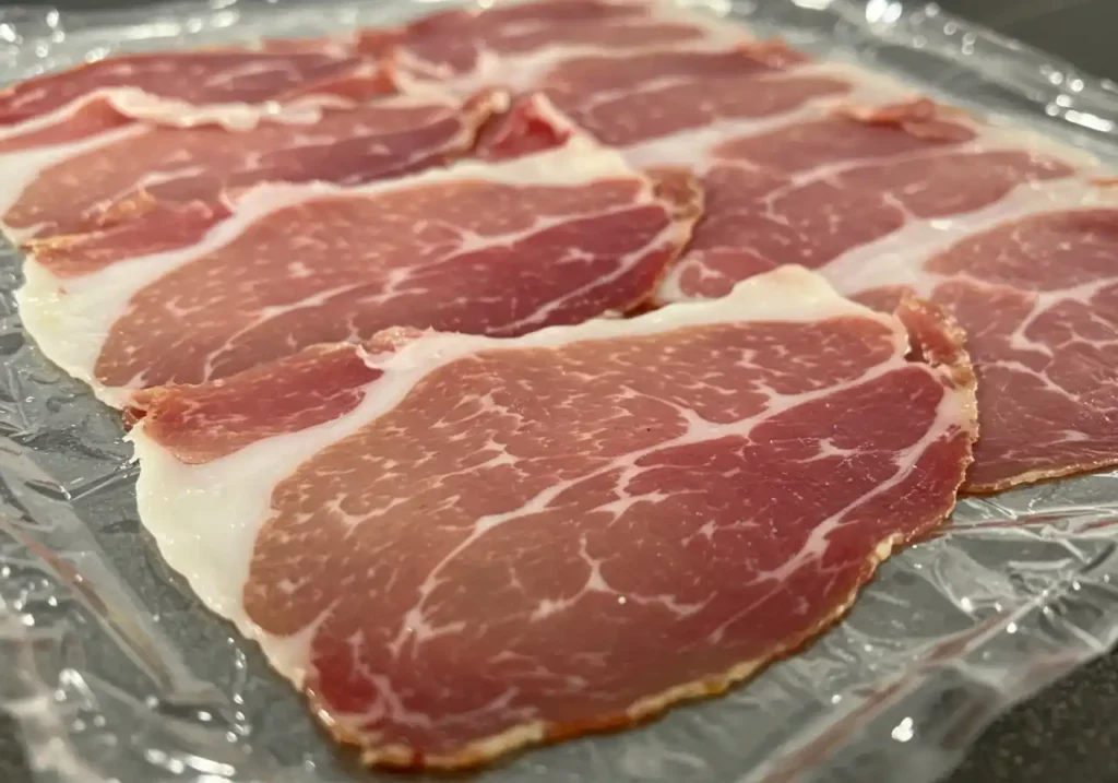 Image montrant la texture et le persillage de tranches de prosciutto cru sur un emballage transparent